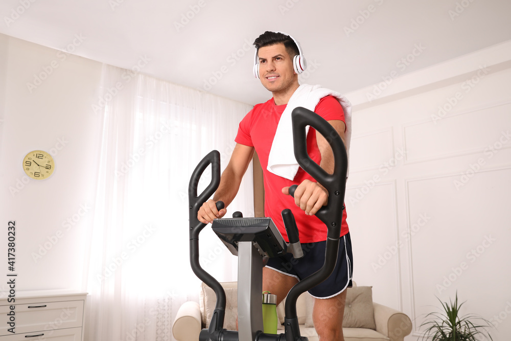 Canvas Prints Man with headphones and towel using modern elliptical machine at home