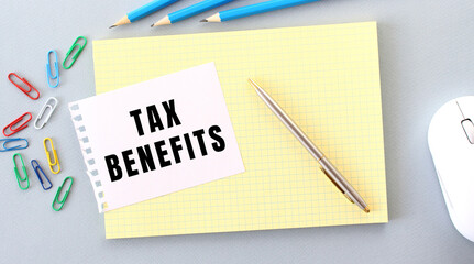 TAX BENEFITS is written on a piece of paper that lies on a notebook next to office supplies.