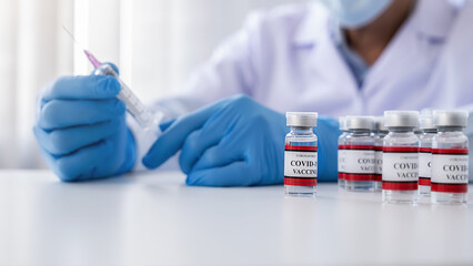 Covid-19 coronavirus vaccine bottles on white table with doctor filling syringe medication background. Fight against Covid-19 coronavirus Concept.