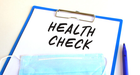 A clipboard with medical protective mask lies on a table. Inscription HEALTH CHECK.