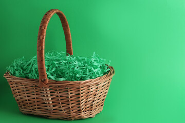 Fototapeta na wymiar Easter basket with bright paper filler on green background, space for text