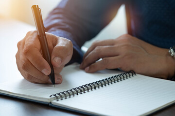 Close-up of man hand using writing pen memo on notebook paper or letter, diary on table desk office. Workplace for student, writer with copy space. business working and learning education concept. - obrazy, fototapety, plakaty