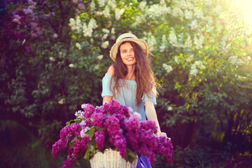 Naklejka premium Portrait of a happy beautiful young girl with vintage bicycle and flowers on city background in the sunlight outdoor. Bike with basket full of flowers. Active Leisure Concept.
