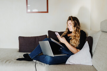 Young woman using smartphone and laptop at home