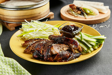 Peking duck chinese food. Yellow plate with vegetables and sauce on dark slate table. Chinese, asian, authentic food concept