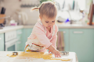 Adorable baby in an apron makes cookies from dough in the kitchen