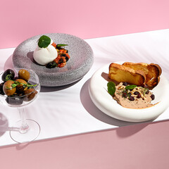 Restaurant appetizers on white table with pink wall. Day sunlight with hard shadow of fern palm leaves. Summer or spring restaurant food concept.