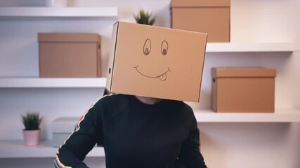Young happy woman with a cardboard box over head with drawn emoji dancing in the new apartment