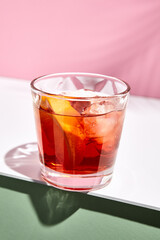 Negroni cocktail over pink background. Drink in rox glass in daylight with palm leaf hard shadow. Summer, tropical, fresh drink concept