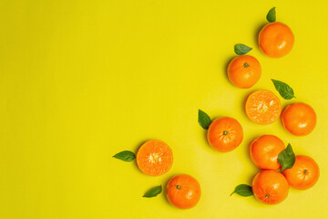 Ripe juicy tangerines and fresh leaves on yellow summer background