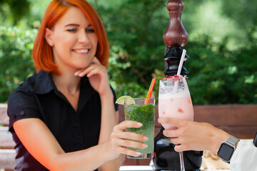 Two young beautiful smiling girls in trendy summer clothes in cafe on the street