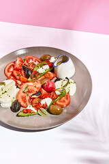 Tomato, olives and mozzarella salad . Restaurant appetizer plate on white table with pink wall. Day sunlight with hard shadow of fern palm leaves. Summer or spring restaurant food concept