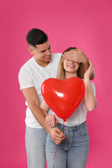 Fototapeta na wymiar Man surprising his girlfriend with heart shaped balloon on pink background. Valentine's day celebration