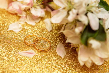 Obraz na płótnie Canvas Gold wedding rings and Apple blossoms on a Golden background 