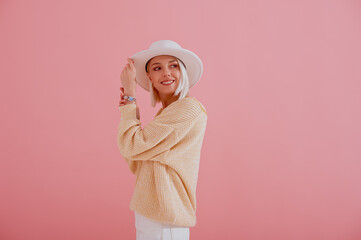 Happy smiling woman wearing trendy yellow sweater, stylish silver wrist watch, white hat posing on pink background. Spring fashion conception. Copy, empty space for text
