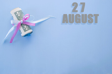 calendar date on blue background with rolled up dollar bills pinned by blue and pink ribbon with copy space. August 27 is the twenty-seventh day of the month