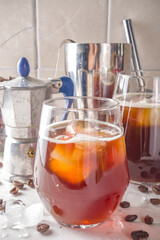 Iced americano espresso coffee without milk, with ice cubes, on white kitchen table background copy space. Black cold brew coffee with ice cubes.