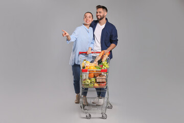Happy couple with shopping cart full of groceries on light grey background © New Africa