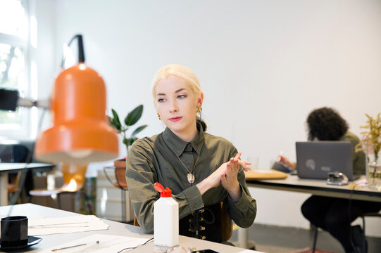 Young Woman Using Hand Sanitizer At Her Desk