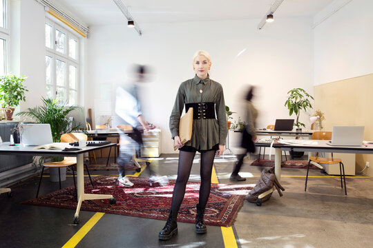 Young woman standing in busy creative co-working space