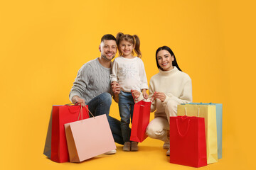 Happy family with paper bags on yellow background. Christmas shopping