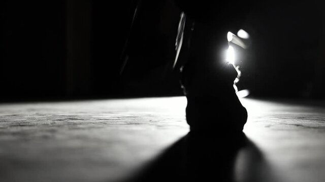 woman high heeled flamenco shoes on a dark floor stepping in flamenco rhythm with back light casting long shadows in the front plane