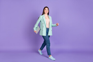 Full length photo of attractive nice young woman walk empty space hold computer smile isolated on violet color background