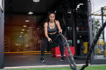 Fototapeta na wymiar Sport. Battle ropes session. Attractive young fit sportswoman working out in functional training gym doing exercise with battle ropes.