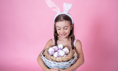 A cute little girl dressed in Easter bunny ears and in a dress posing with a basket of Easter eggs.