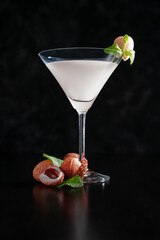 An elegant lychee drink decorated with lychee fruit. Drink in a martini glass. Drink on a black...