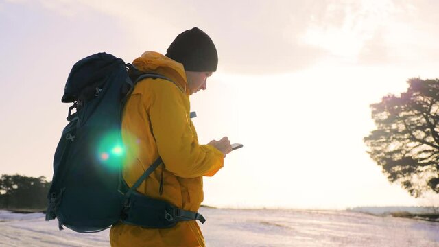 Man hiker backpacker, traveler camper with her phone looks at a map or route under sun light. Hiking, backpacking on winter.
