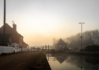 Fototapeta na wymiar Sawley Marina, Trent Lock Nottingham 29th Feb 2020 two canal locks with keepers cottage on waterway . Foggy misty morning as sun rises giving beautiful bright golden light.