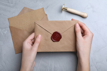 Woman holding envelope with wax seal at grey table, top view