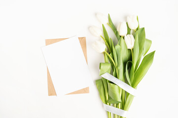 Fresh cut white tulip flowers and blank card with envelope top view on white background with copy space