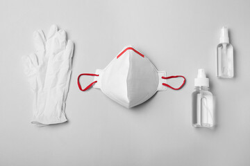 Medical gloves, respiratory mask and hand sanitizers on grey background, flat lay