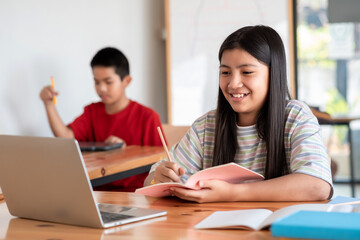 Obraz premium Young Asian girl happy online learning using laptop and taking notes in the classroom.