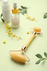Natural face roller, cosmetic products and flowers on green background