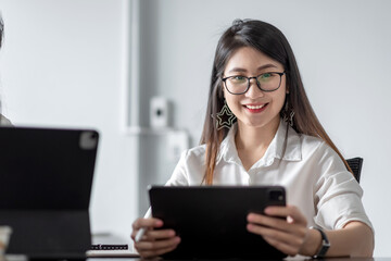 Charming Asian woman holding a tablet in the office. Looking at the camera.