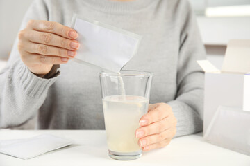 Woman pouring powder from medicine sachet into glass with water at table, closeup - obrazy, fototapety, plakaty