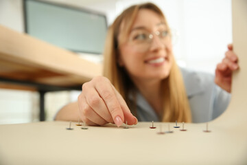 Young woman putting pins on colleague's chair in office. Funny joke