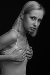 Obraz premium black and white portrait of a blonde on a black background. in a white tank top with straps. holding on to the chest
