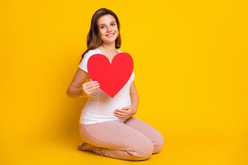Photo of sweet pretty woman expecting child wear white outfit hugging belly holding red heart isolated yellow color background