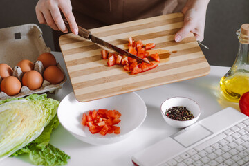 Woman blogger preparing diet vegetable salad. Online cooking lessons, using a laptop in the kitchen. Record cooking recipes on camera.