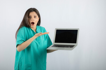 Young female nurse with laptop surprised about something on white background