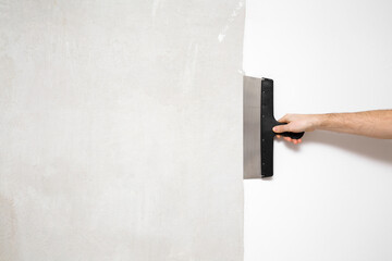 Young adult man hand using spatula and plastering wall with white fresh finishing putty. Closeup....