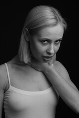 Fototapeta premium black-and-white portrait of a blonde on a black background. in a white tank top with straps strangles, holds a hand to his neck