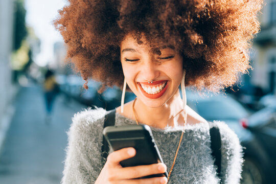 Young woman looking at phone outdoors, smiling