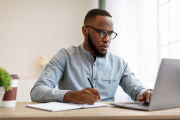 Obraz premium Serious Black Man Writing Business Report At Laptop In Office