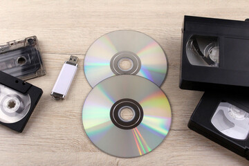 Compact discs, cassettes and a USB flash drive on a wooden background. Information recording technologies