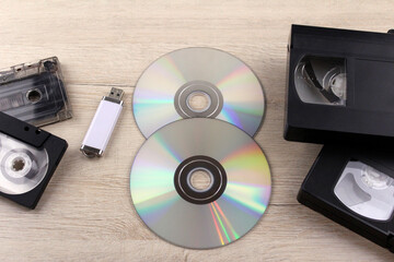 Compact discs, cassettes and a USB flash drive on a wooden background. Information recording...